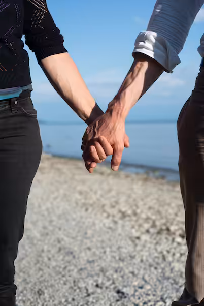 Zwei Menschen halten sich am Strand an den Händen