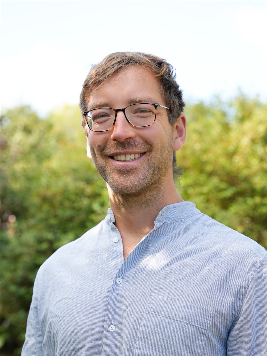 Vincent Schmock, lächelnd, im Garten vor grünen Büschen